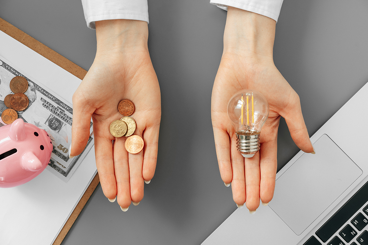 Hands holding pennies on the left side, and a light bulb on the right.